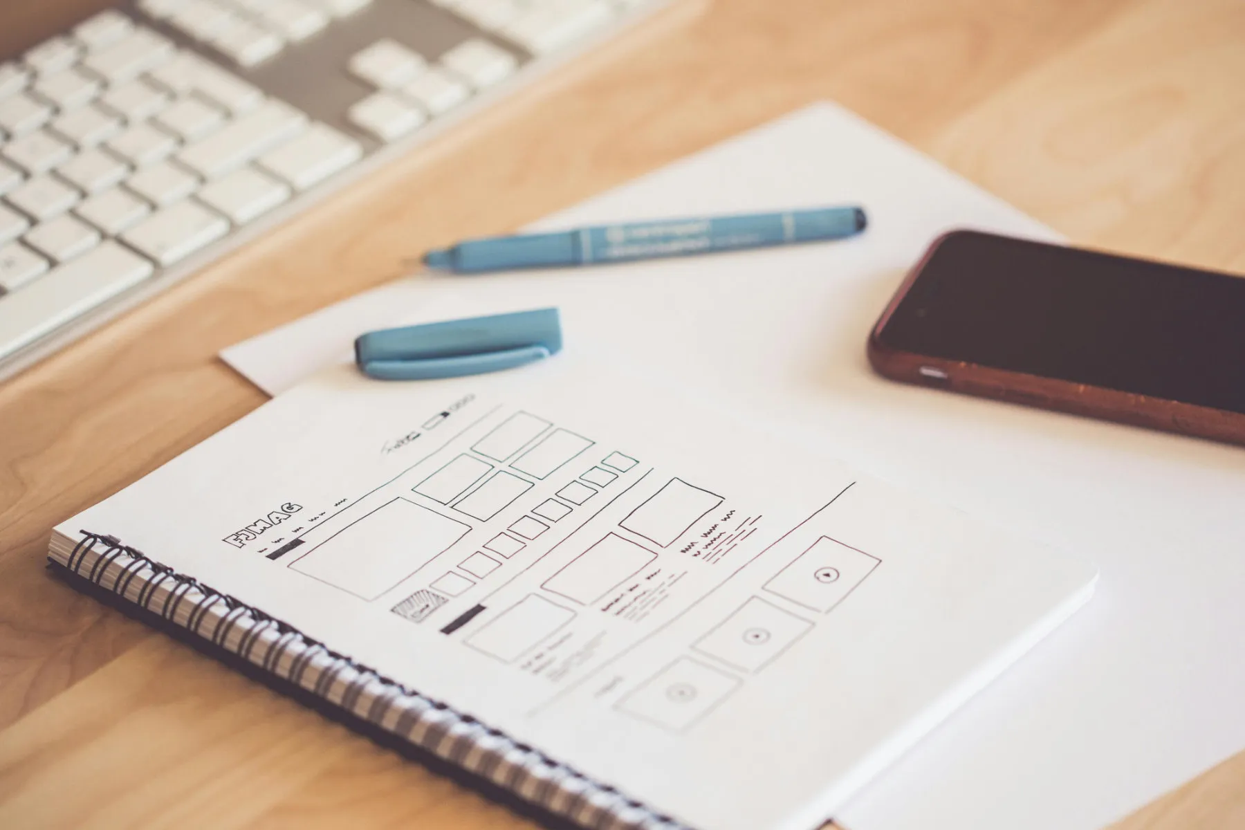 Hand-sketched website wireframe in a notebook beside a keyboard and phone.