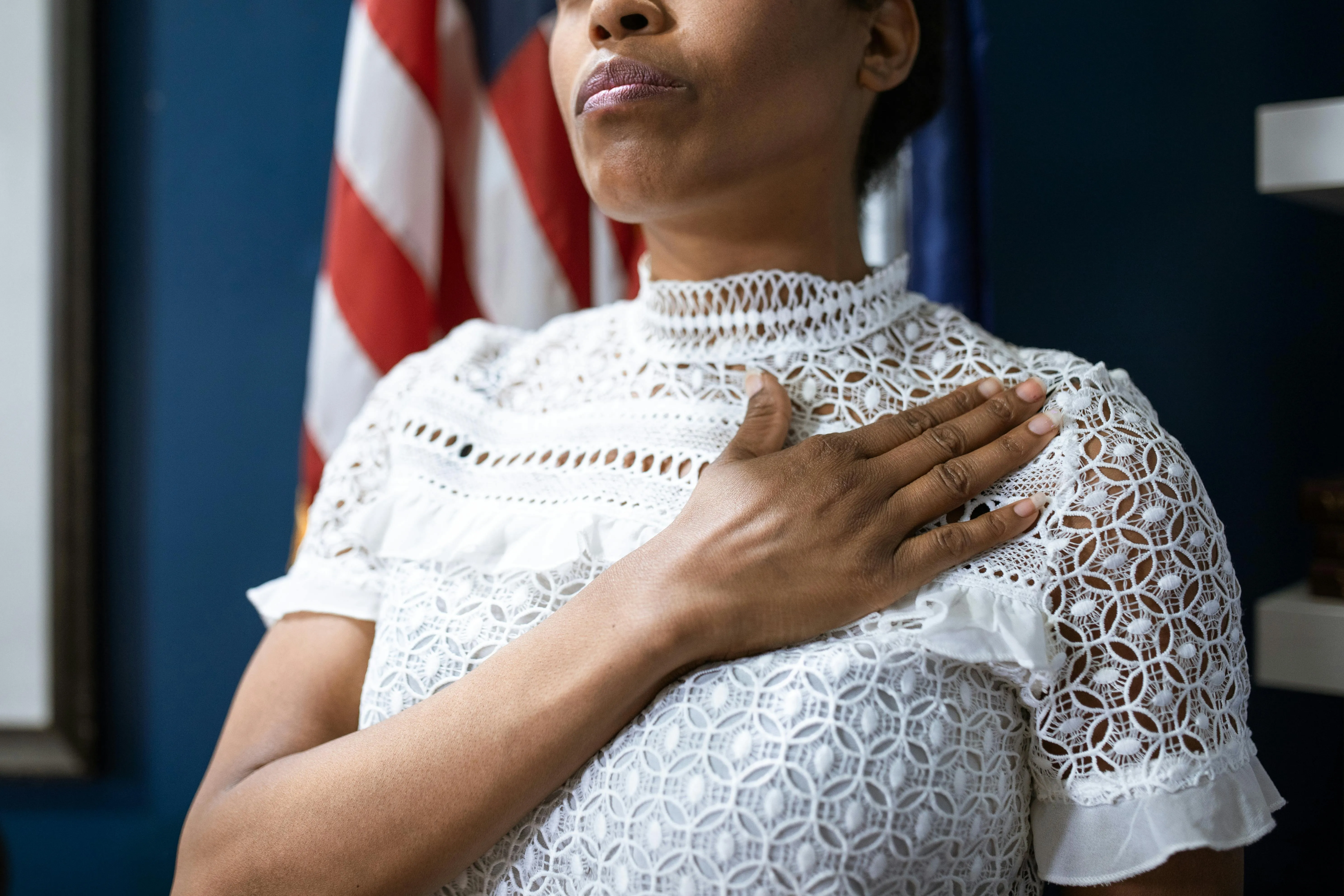 A woman with her hand on her chest during a naturalization oath ceremony, a US flag behind her.
